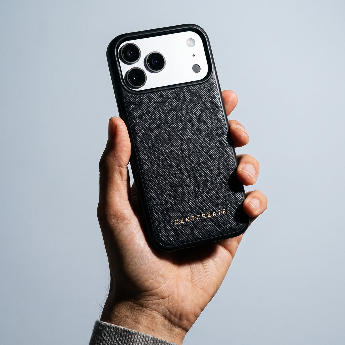 Hand holding a black Saffiano cross-hatch calfskin iPhone 18 Pro Max case by GENTCREATE against pale grey