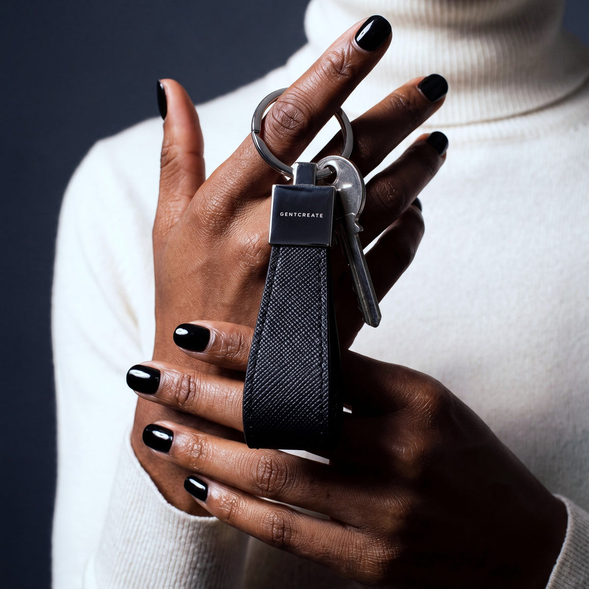 Hands holding a black Saffiano leather keychain by GENTCREATE with house keys