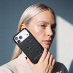 امرأة تمسك جرابًا أسود لهاتف iPhone 18 Pro Max من جلد عجل بنقش موجي بارز من GENTCREATE مسندًا إلى خدها تحت ضوء النافذة