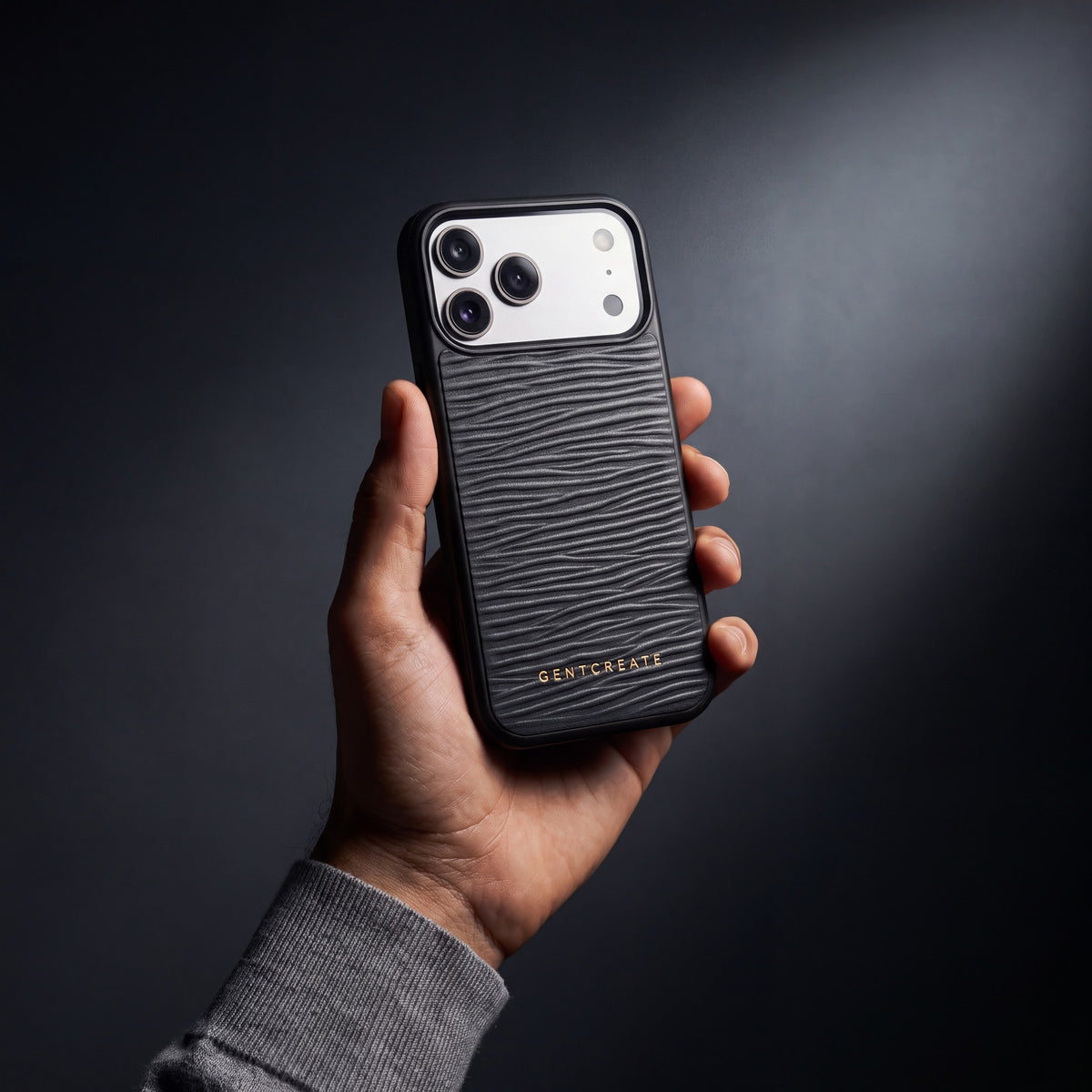 يد رجل تمسك جراب أسود لهاتف iPhone 18 Pro Max من جلد عجل بنقش موجي بارز من GENTCREATE في استوديو مظلم