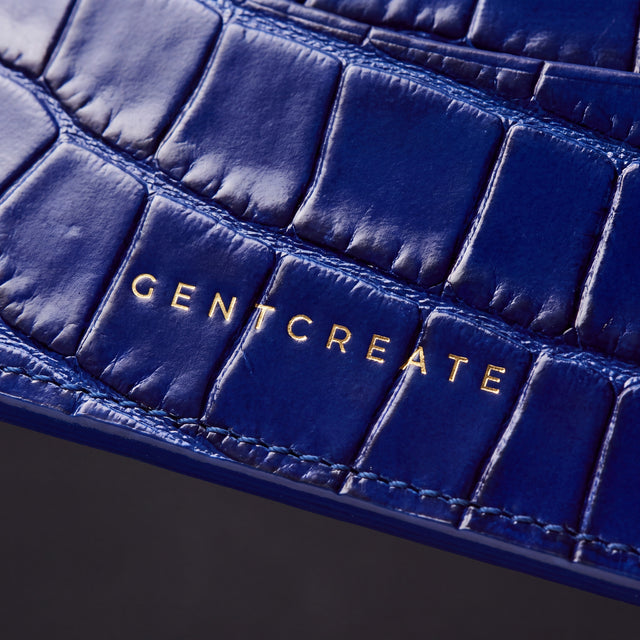 Κοντινό πλάνο της χρυσής σφραγίδας GENTCREATE σε μπλε καρτοθήκη από γυαλιστερό δέρμα με ανάγλυφο κροκό