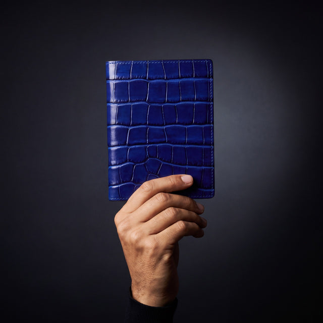 Mão masculina a segurar um porta-passaporte da GENTCREATE em pele azul brilhante gravada efeito croco, em estúdio escuro