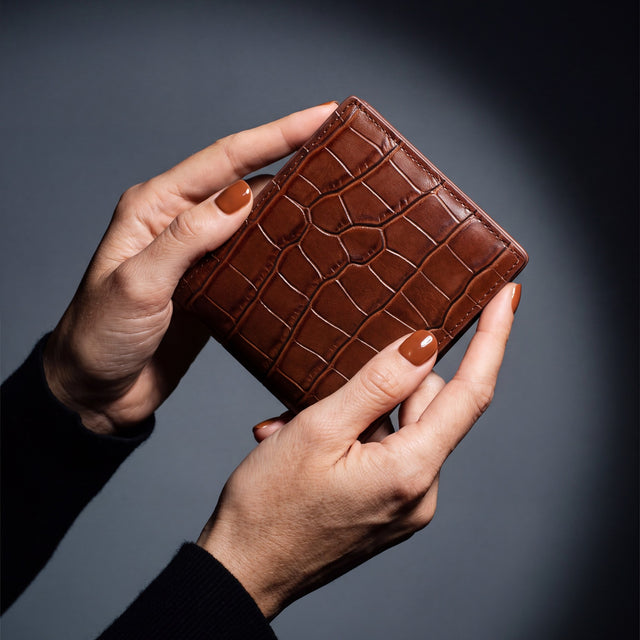 Close-up of hands holding a brown crocodile-embossed leather bifold wallet by GENTCREATE