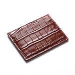 Brown crocodile-embossed leather card holder by GENTCREATE lying at an angle on white