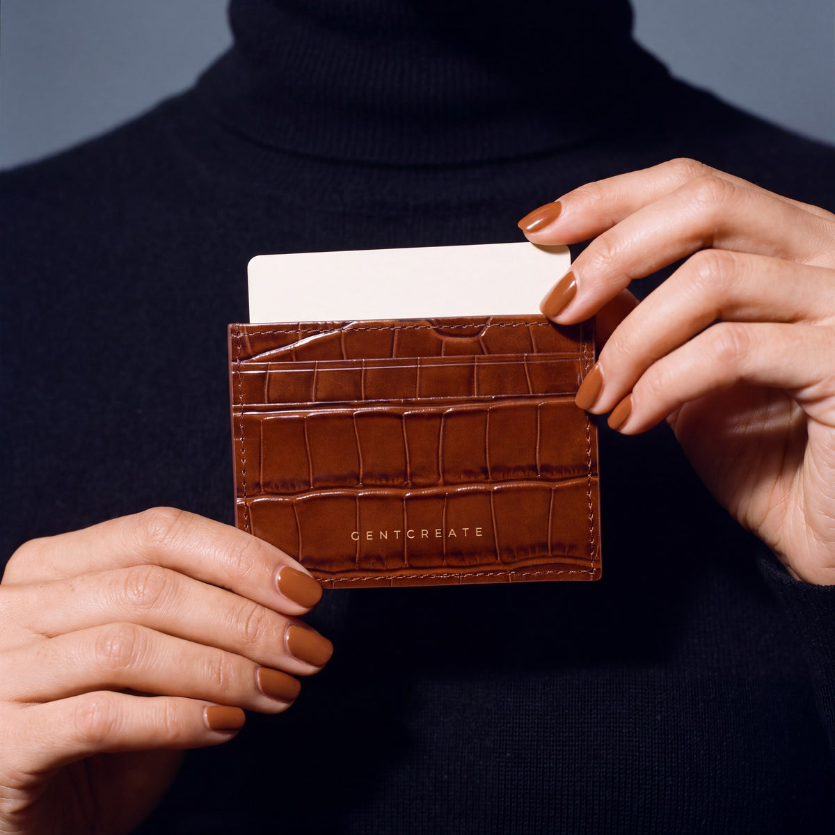 Close-up of hands holding a brown crocodile-embossed leather card holder by GENTCREATE with a card in the top slot