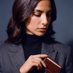 Woman slipping a brown crocodile-embossed leather card holder by GENTCREATE into a blazer chest pocket