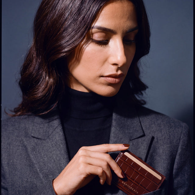 Woman slipping a brown crocodile-embossed leather card holder by GENTCREATE into a blazer chest pocket