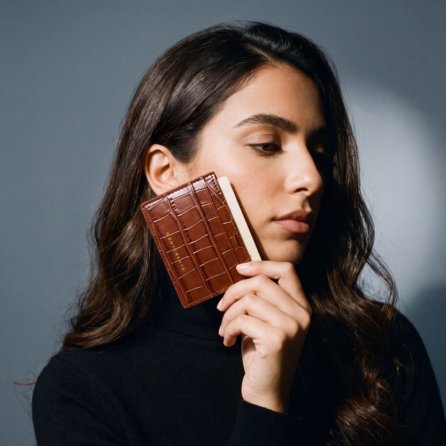 Woman holding a slim brown crocodile-embossed leather card holder by GENTCREATE and drawing out a card