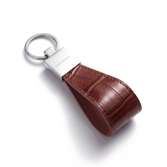 Brown crocodile-embossed leather keychain by GENTCREATE lying at an angle on white