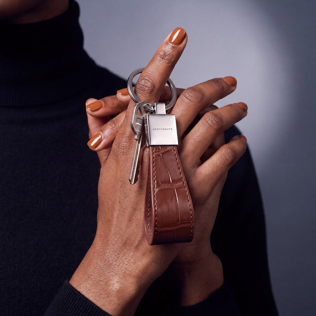 Close-up of a brown crocodile-embossed leather keychain by GENTCREATE with house keys hanging from a finger