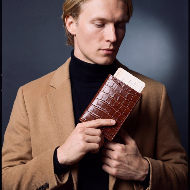 Man holding a brown crocodile-embossed leather passport holder by GENTCREATE with a blank card tucked in