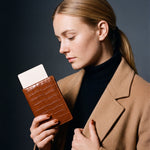 Woman holding a brown crocodile-embossed leather passport holder by GENTCREATE with a blank card tucked in