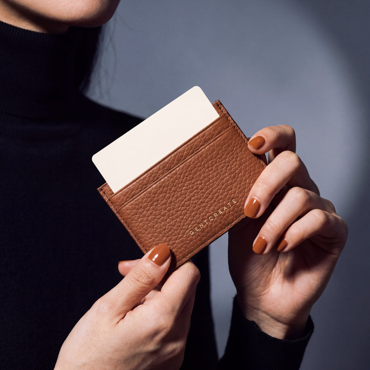 Close-up of hands holding a brown pebble leather card holder by GENTCREATE with a card in the top slot