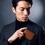 Man slipping a brown pebble leather card holder by GENTCREATE into a blazer chest pocket