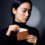 Woman sliding a card into a brown pebble leather card holder by GENTCREATE