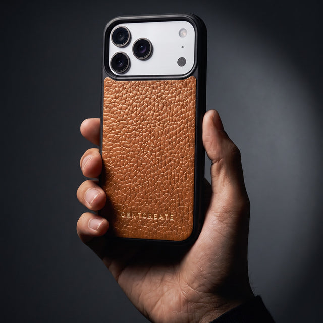 Hand holding a brown pebble-grain leather iPhone 18 Pro Max case by GENTCREATE in a single studio light