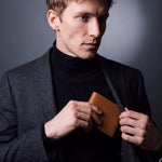 Man sliding a brown Saffiano leather bifold wallet by GENTCREATE into a blazer pocket