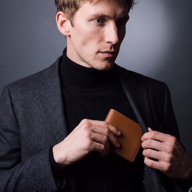 Man sliding a brown Saffiano leather bifold wallet by GENTCREATE into a blazer pocket