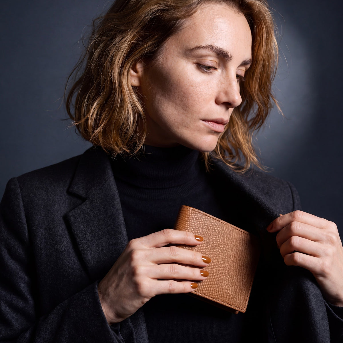 Woman sliding a brown Saffiano leather bifold wallet by GENTCREATE into a blazer pocket