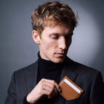 Man slipping a brown Saffiano leather card holder by GENTCREATE into a blazer chest pocket