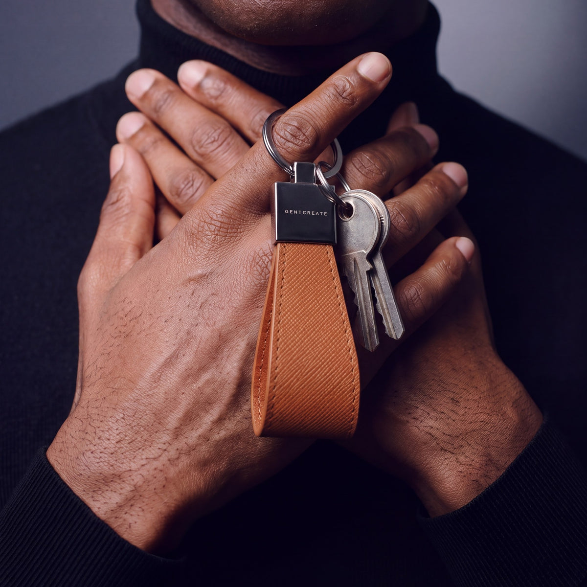 Close-up of a brown Saffiano leather keychain by GENTCREATE with house keys hanging from a finger