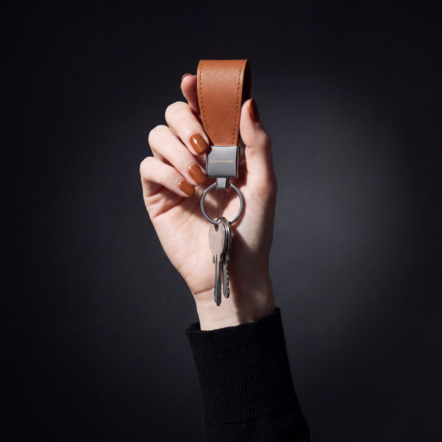 어두운 스튜디오에서 열쇠를 단 GENTCREATE 브라운 Saffiano 가죽 키링을 들어 보이는 여성의 손