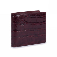 Closed burgundy crocodile-embossed leather bifold wallet by GENTCREATE standing on white