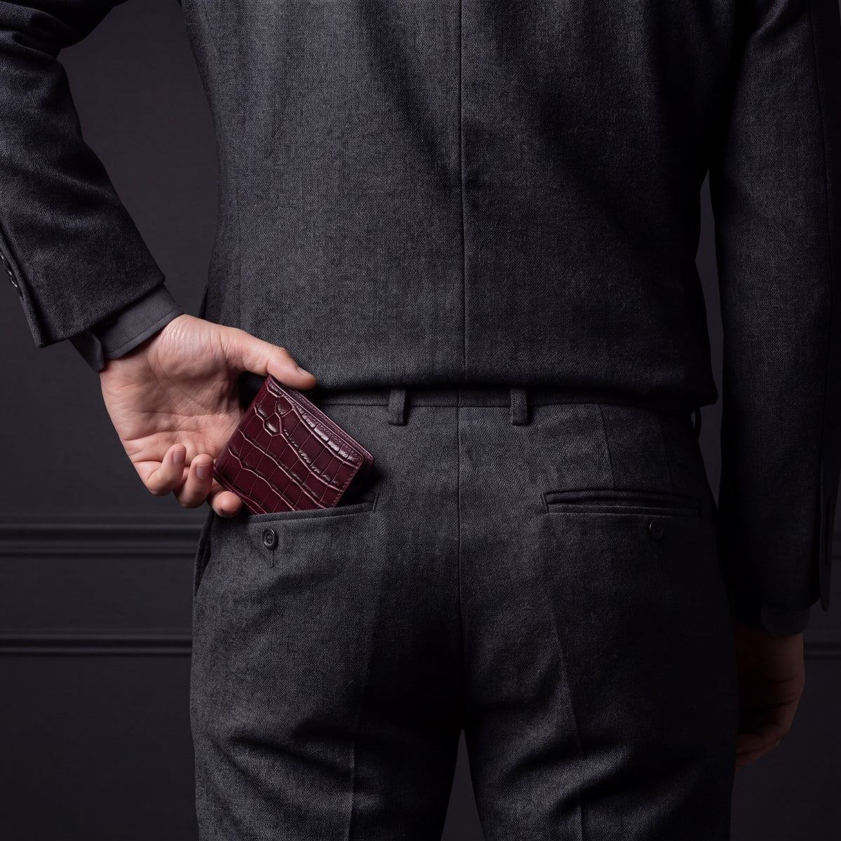 Man sliding a burgundy crocodile-embossed leather bifold wallet by GENTCREATE into his back trouser pocket