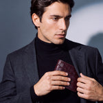 Man sliding a burgundy crocodile-embossed leather bifold wallet by GENTCREATE into a blazer pocket