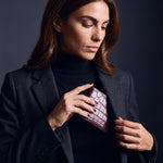 Woman sliding a burgundy crocodile-embossed leather bifold wallet by GENTCREATE into a blazer pocket