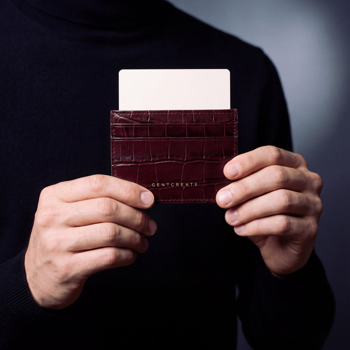 Close-up of hands holding a burgundy crocodile-embossed leather card holder by GENTCREATE with a card in the top slot