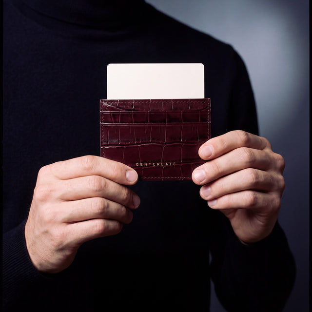Close-up of hands holding a burgundy crocodile-embossed leather card holder by GENTCREATE with a card in the top slot