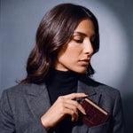 Woman slipping a burgundy crocodile-embossed leather card holder by GENTCREATE into a blazer chest pocket