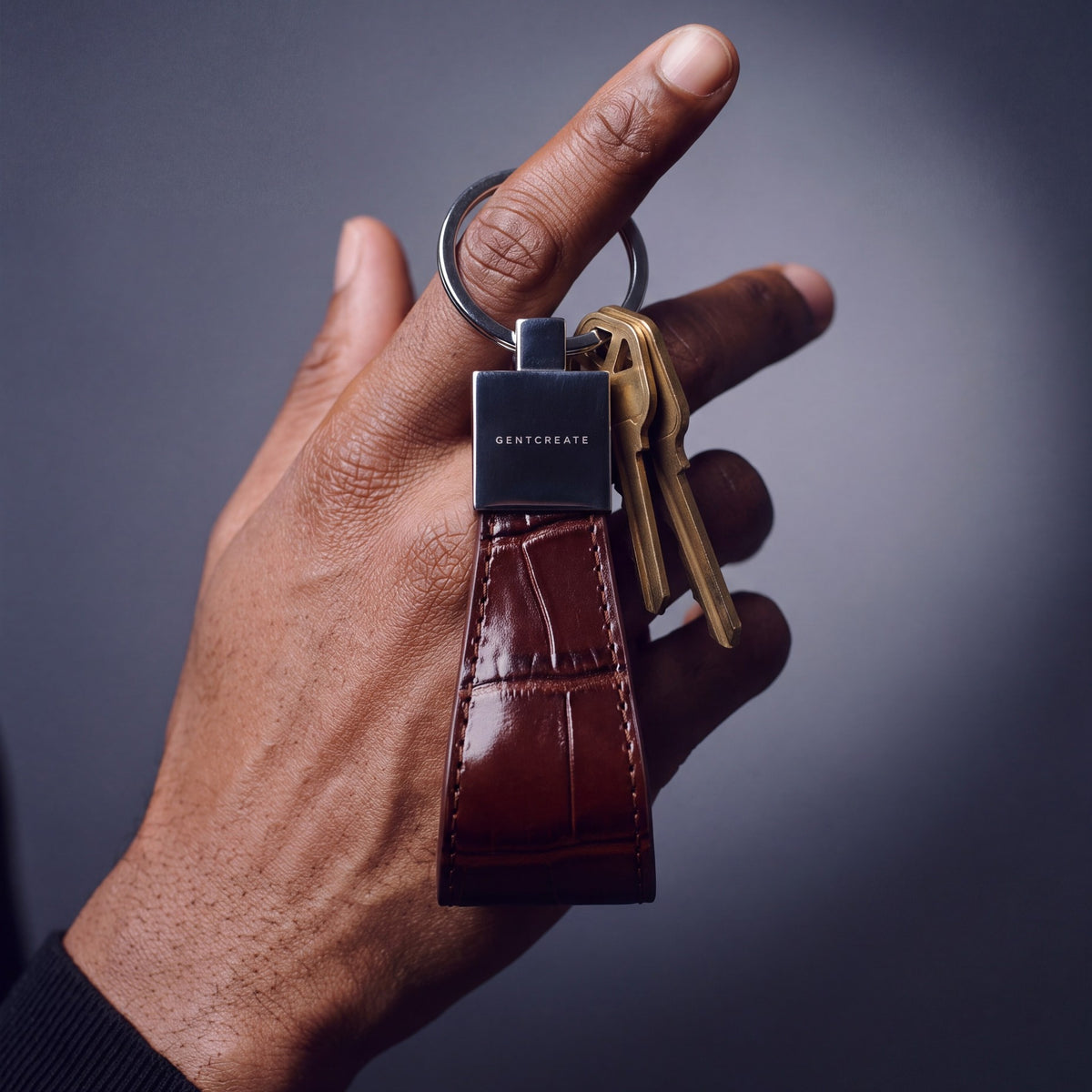 Close-up of a burgundy crocodile-embossed leather keychain by GENTCREATE with house keys hanging from a finger