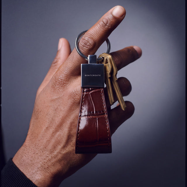Close-up of a burgundy crocodile-embossed leather keychain by GENTCREATE with house keys hanging from a finger