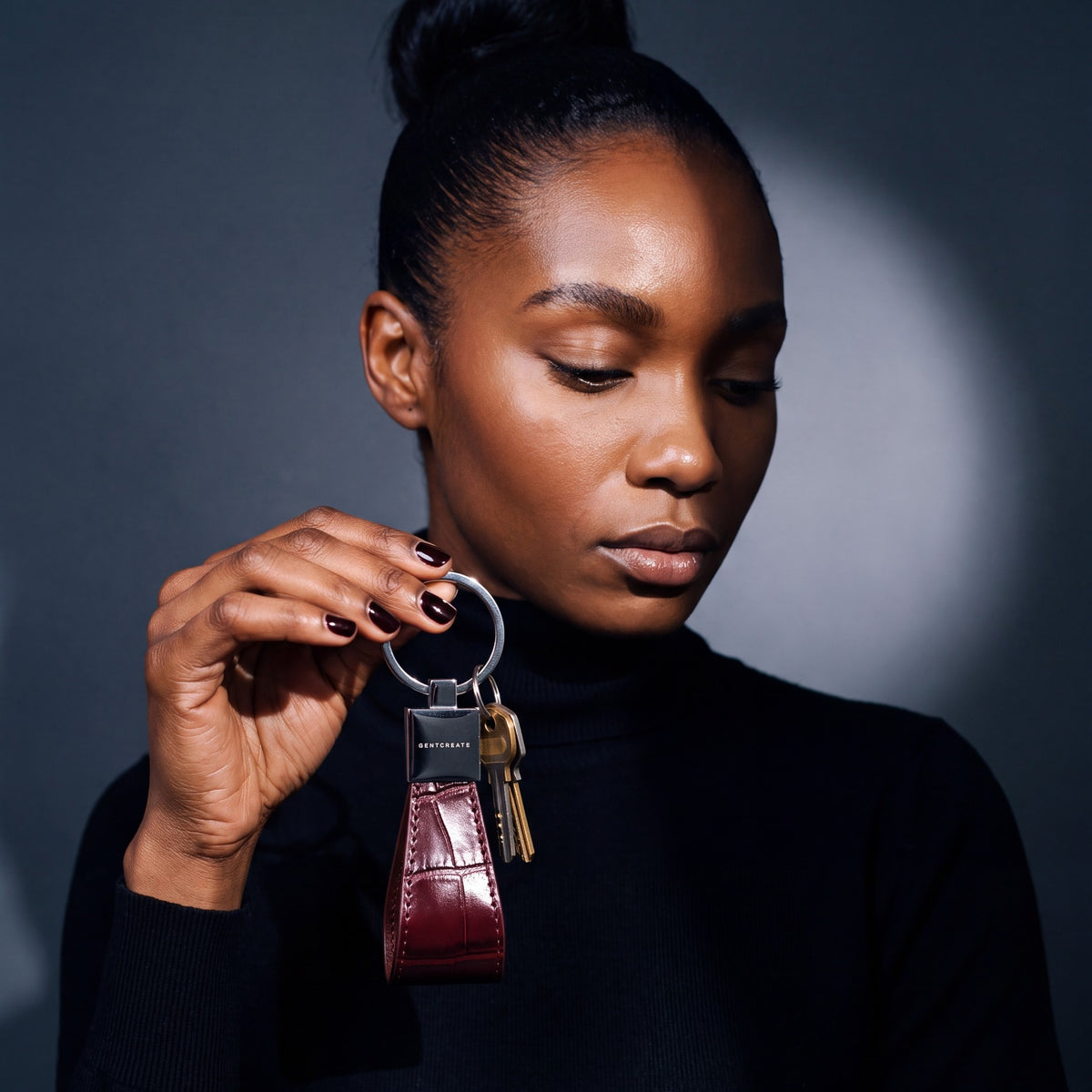 Woman holding up a burgundy crocodile-embossed leather keychain by GENTCREATE with house keys