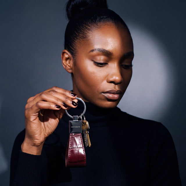 Woman holding up a burgundy crocodile-embossed leather keychain by GENTCREATE with house keys