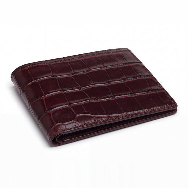Closed burgundy glossy crocodile-embossed leather bifold wallet by GENTCREATE lying on white