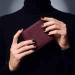 Close-up of hands holding a burgundy lizard-embossed leather bifold wallet by GENTCREATE