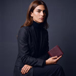 Woman seated, holding a burgundy lizard-embossed leather bifold wallet by GENTCREATE