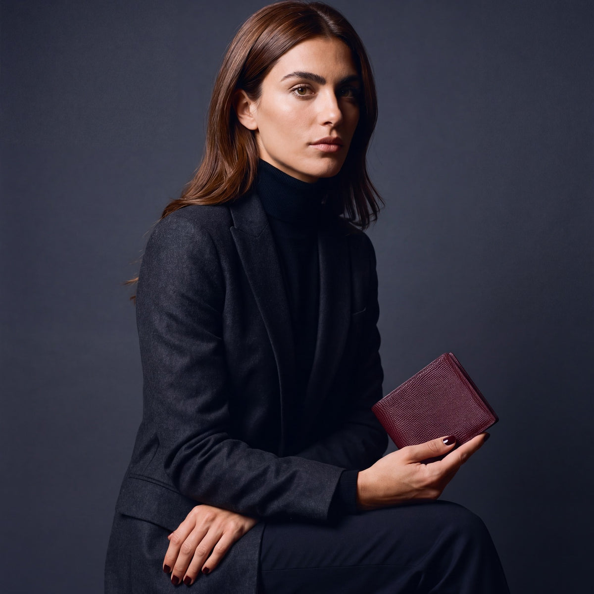 Woman seated, holding a burgundy lizard-embossed leather bifold wallet by GENTCREATE