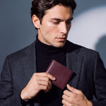 Man sliding a burgundy lizard-embossed leather bifold wallet by GENTCREATE into a blazer pocket