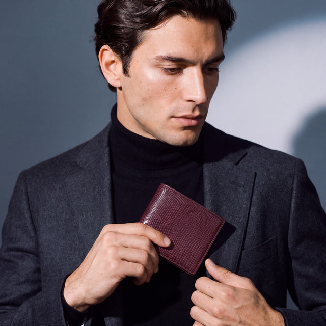 Man sliding a burgundy lizard leather bifold wallet by GENTCREATE into a blazer pocket