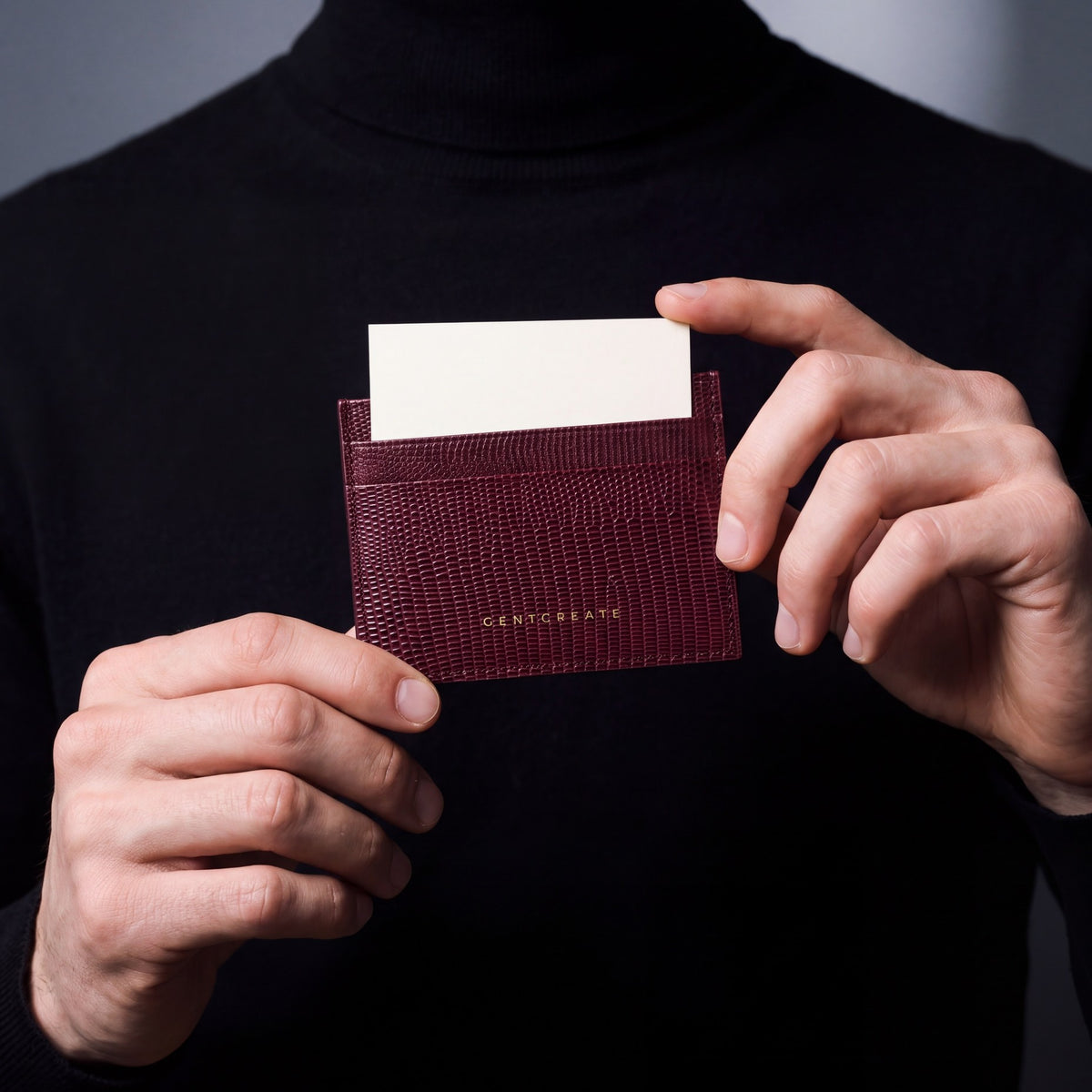 Close-up of hands holding a burgundy lizard-embossed leather card holder by GENTCREATE with a card in the top slot