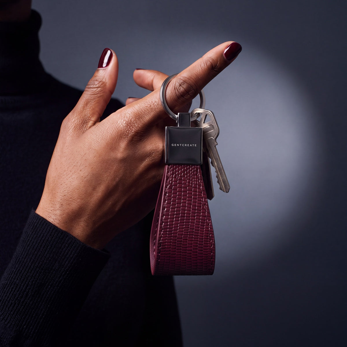 Close-up of a burgundy lizard-embossed leather keychain by GENTCREATE with house keys hanging from a finger
