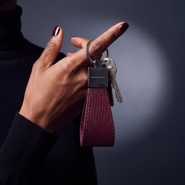 Close-up of a burgundy lizard-embossed leather keychain by GENTCREATE with house keys hanging from a finger