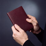 Close-up of hands holding a burgundy lizard-embossed leather passport holder by GENTCREATE