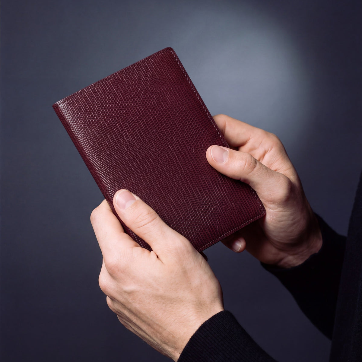 Close-up of hands holding a burgundy lizard-embossed leather passport holder by GENTCREATE