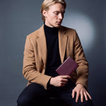 Man seated, holding a burgundy lizard-embossed leather passport holder by GENTCREATE
