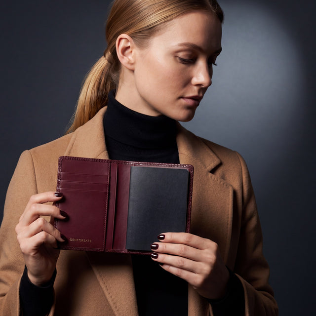 Woman opening a burgundy lizard leather passport holder by GENTCREATE with a passport inside